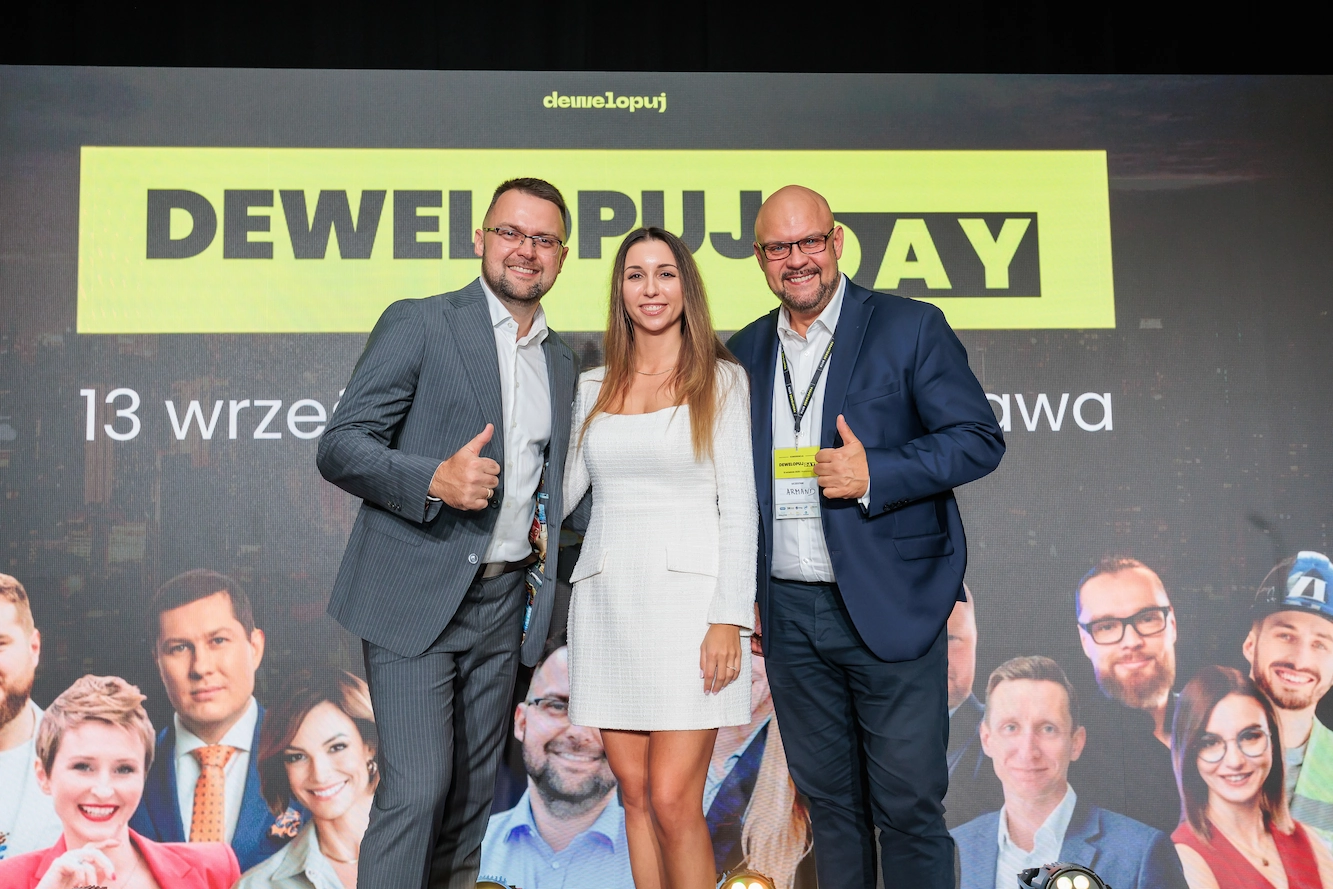 Trzy osoby przy banerze Dewelopuj Day 2025